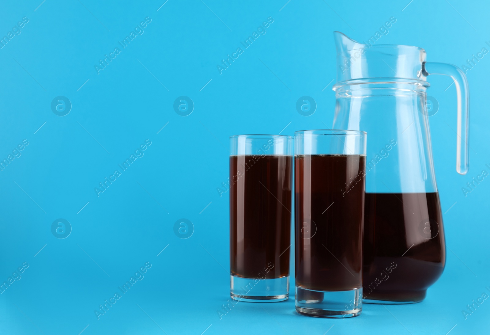 Photo of Delicious homemade kvass in glasses and jug on light blue background. Space for text