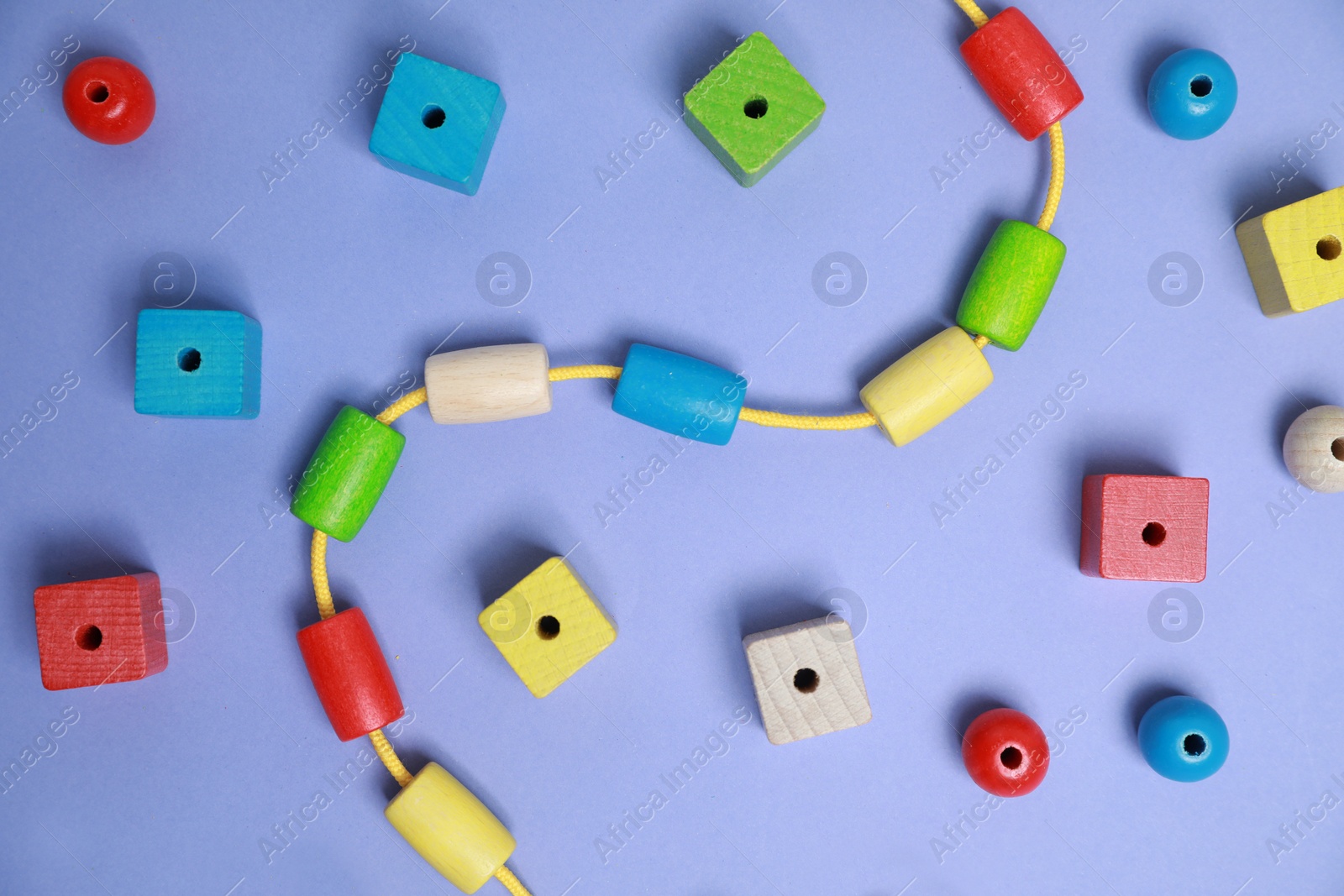 Photo of Wooden pieces and string for threading activity on violet background, flat lay. Educational toy for motor skills development