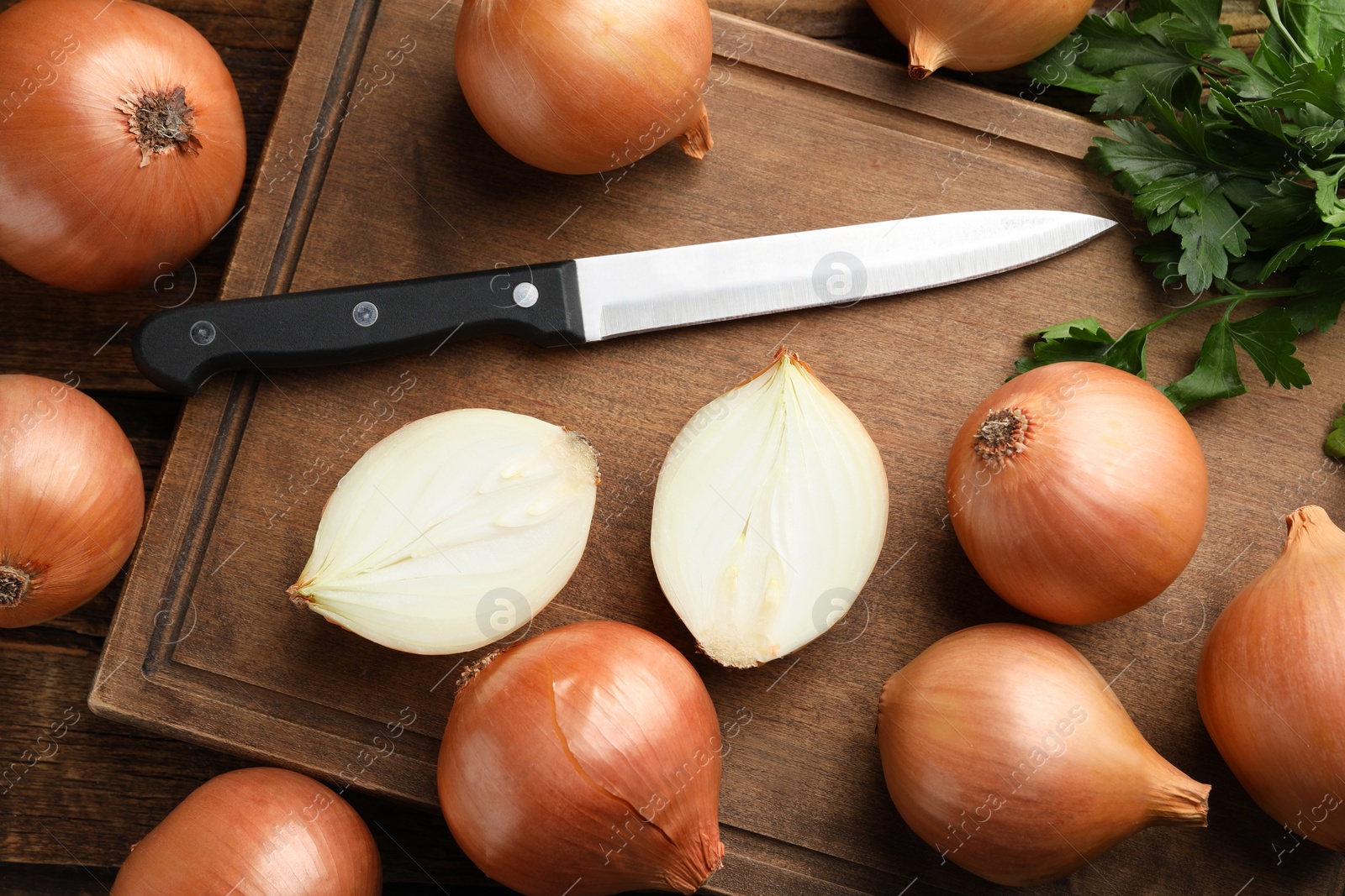 Photo of Whole and cut onions with knife and parsley on wooden table, flat lay