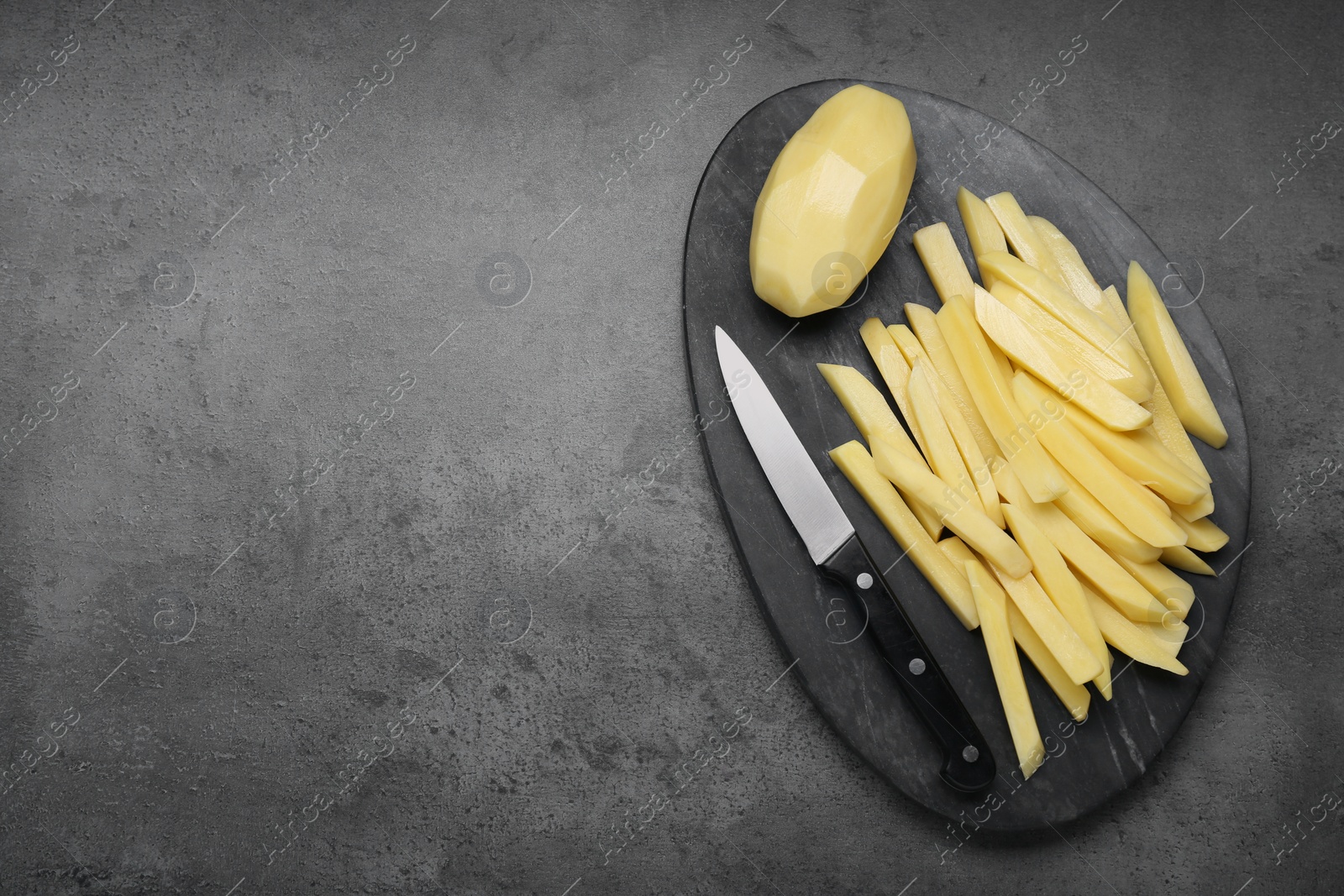 Photo of Whole and cut raw potatoes with knife on grey table, top view. Space for text. Cooking delicious French fries