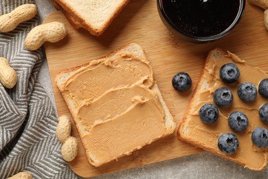 Photo of Tasty peanut butter sandwiches with fresh blueberries, jam and peanuts on table, top view