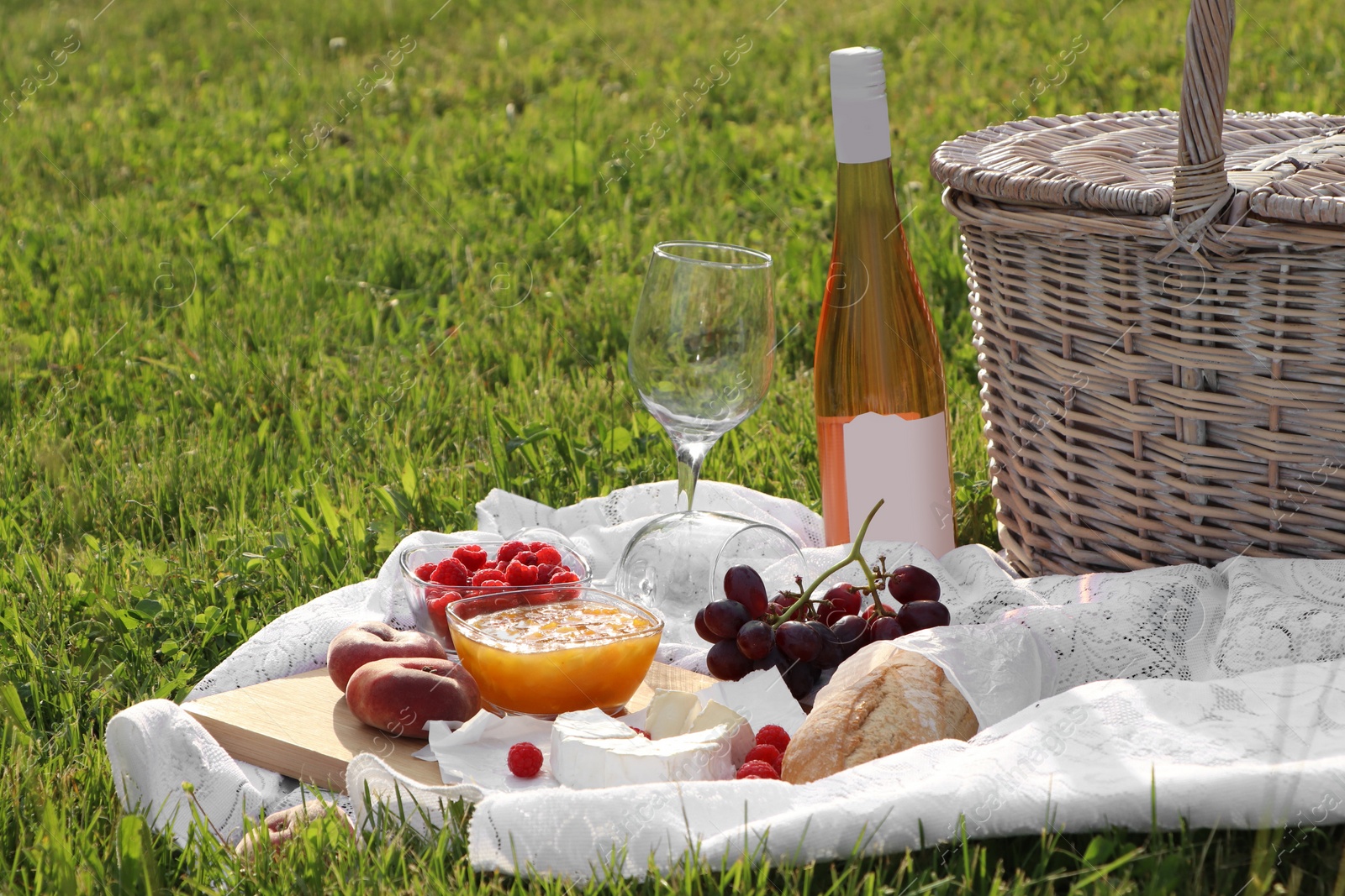 Photo of Picnic blanket with tasty food, basket and cider on green grass outdoors