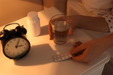 Woman with glass of water and pills in bedroom at night, closeup. Insomnia concept