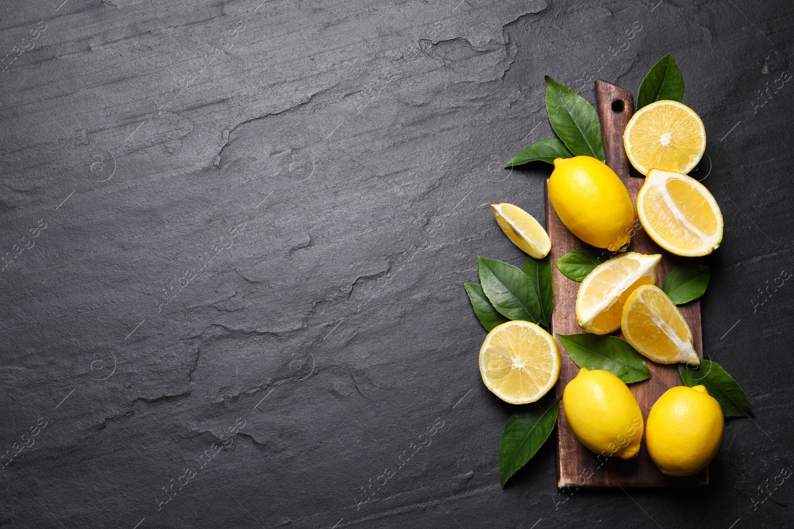 Photo of Many fresh ripe lemons with green leaves on black table, top view. Space for text