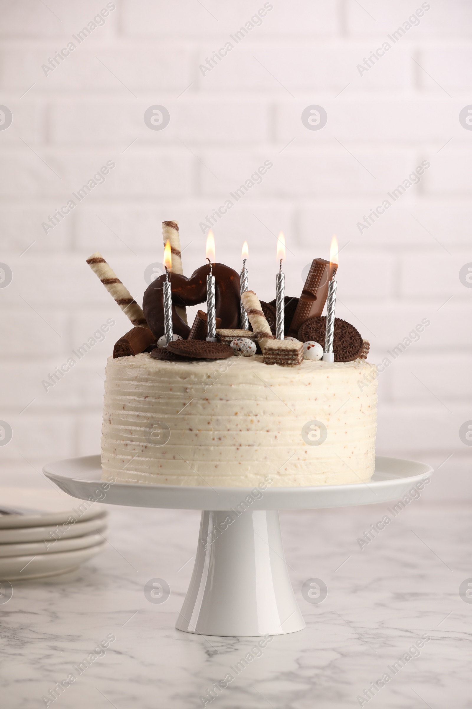 Photo of Delicious cake decorated with sweets and burning candles on white marble table