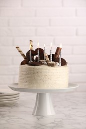 Photo of Delicious cake decorated with sweets and burning candles on white marble table