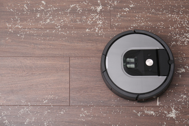 Photo of Removing groats from wooden floor with robotic vacuum cleaner at home, top view. Space for text
