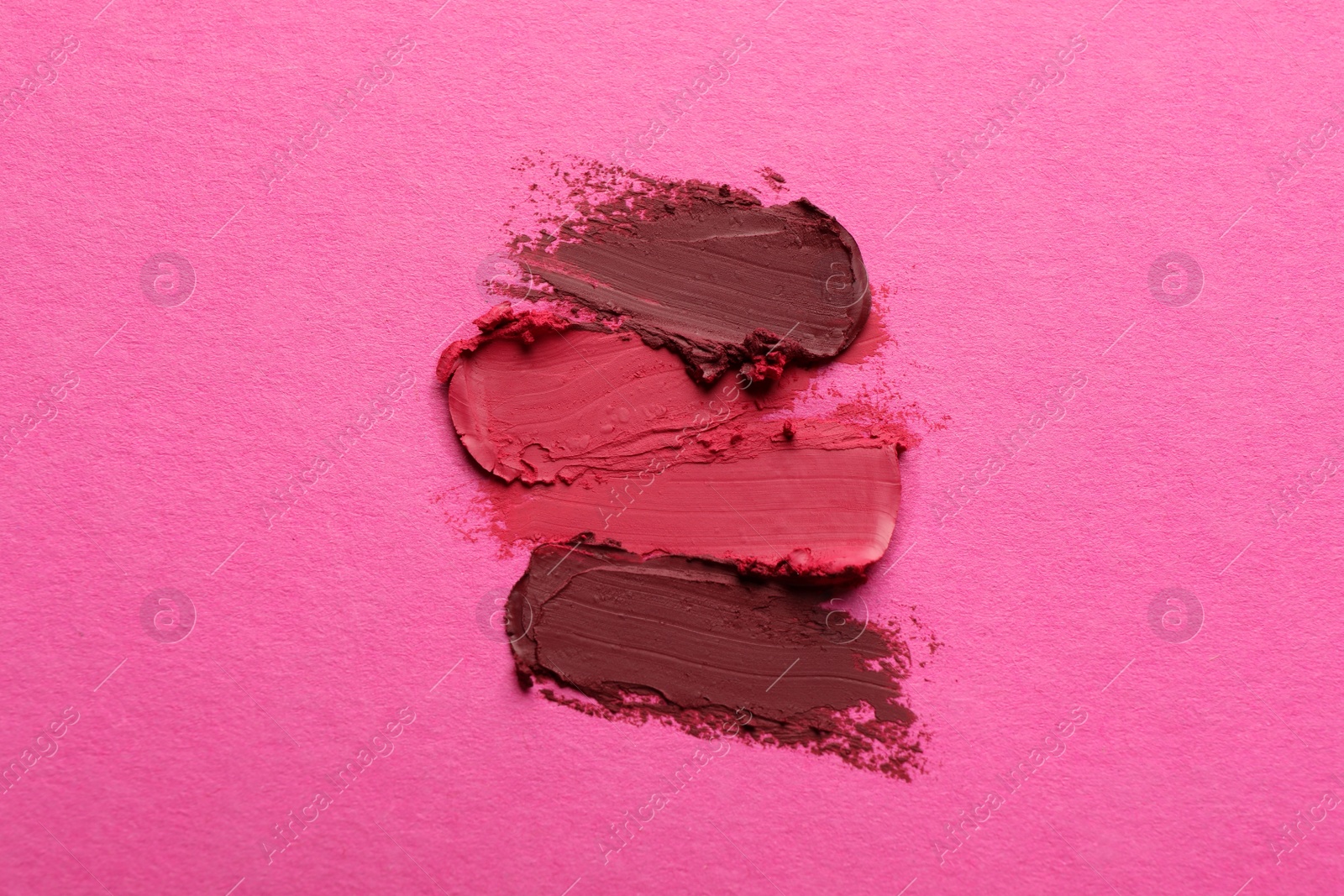 Photo of Smears of beautiful lipsticks on pink background, top view