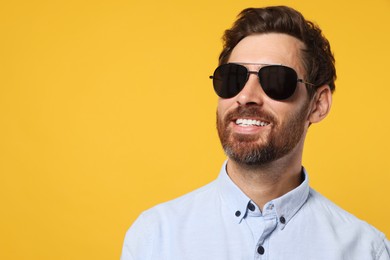 Photo of Portrait of smiling bearded man with stylish sunglasses on orange background. Space for text
