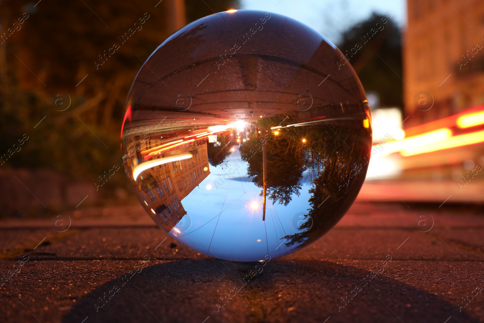 Photo of Beautiful city street, overturned reflection. Crystal ball on asphalt road at night, closeup