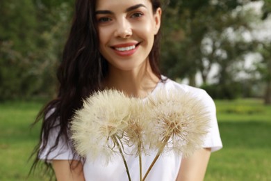 Photo of Beautiful young woman with large dandelions in park, focus on flowers. Allergy free concept