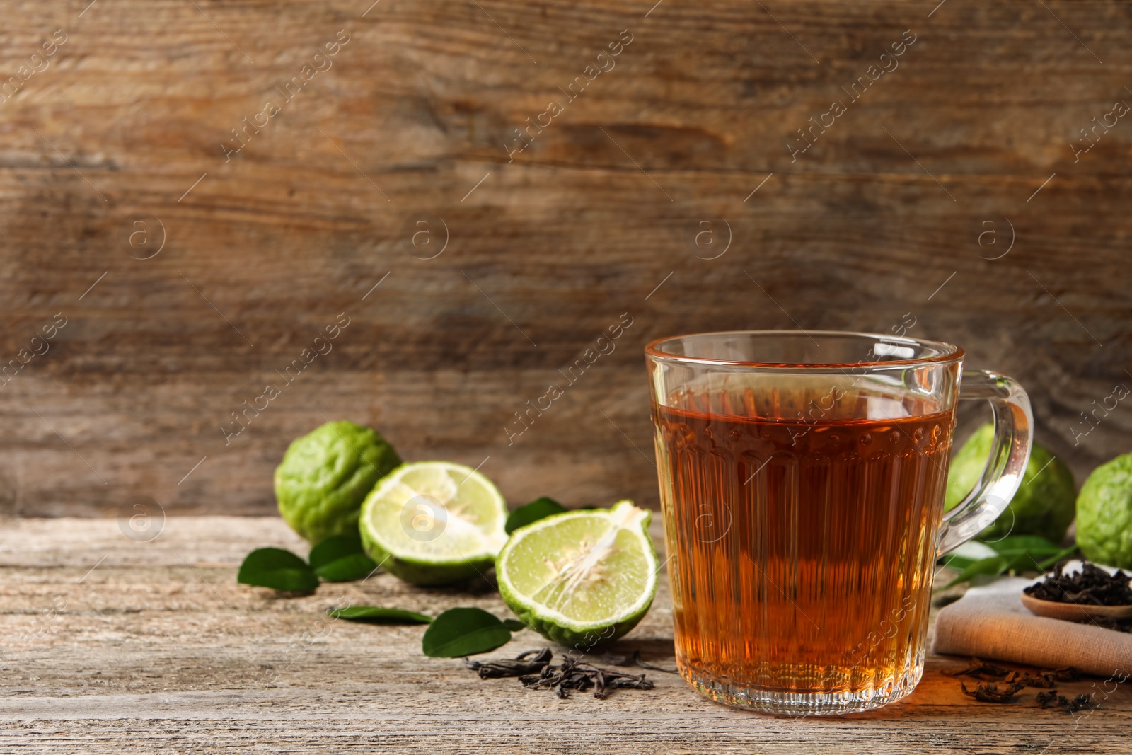 Photo of Glass cup of tasty bergamot tea and fresh fruits on wooden table, space for text