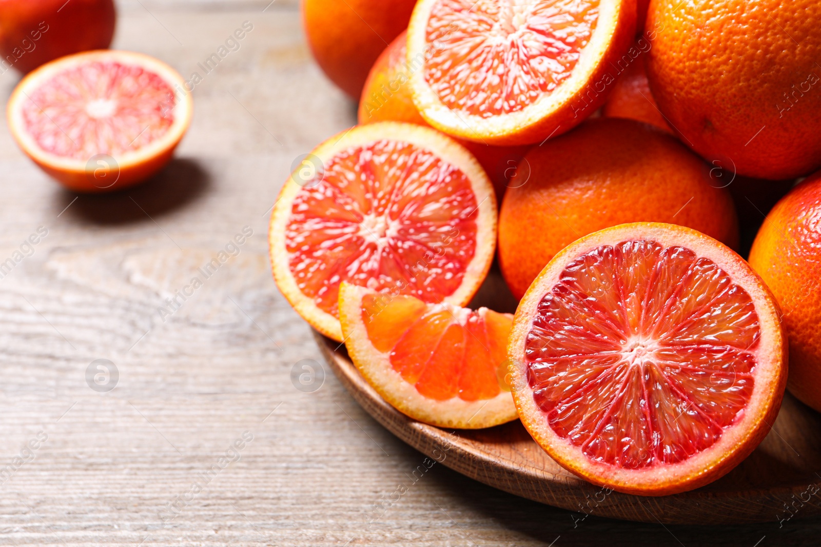 Photo of Whole and cut red oranges on wooden table, closeup