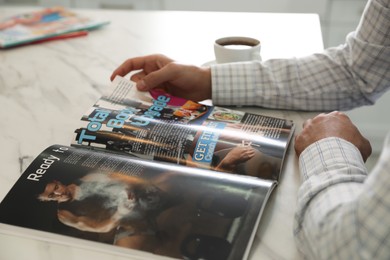 Photo of Man reading sports magazine at white marble table, closeup