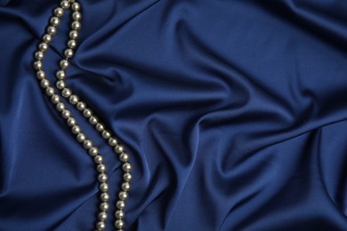 Photo of Beautiful pearls on dark blue silk, top view. Space for text