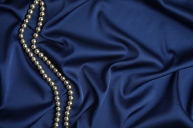 Beautiful pearls on dark blue silk, top view. Space for text