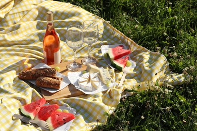 Picnic blanket with delicious food and wine on green grass outdoors