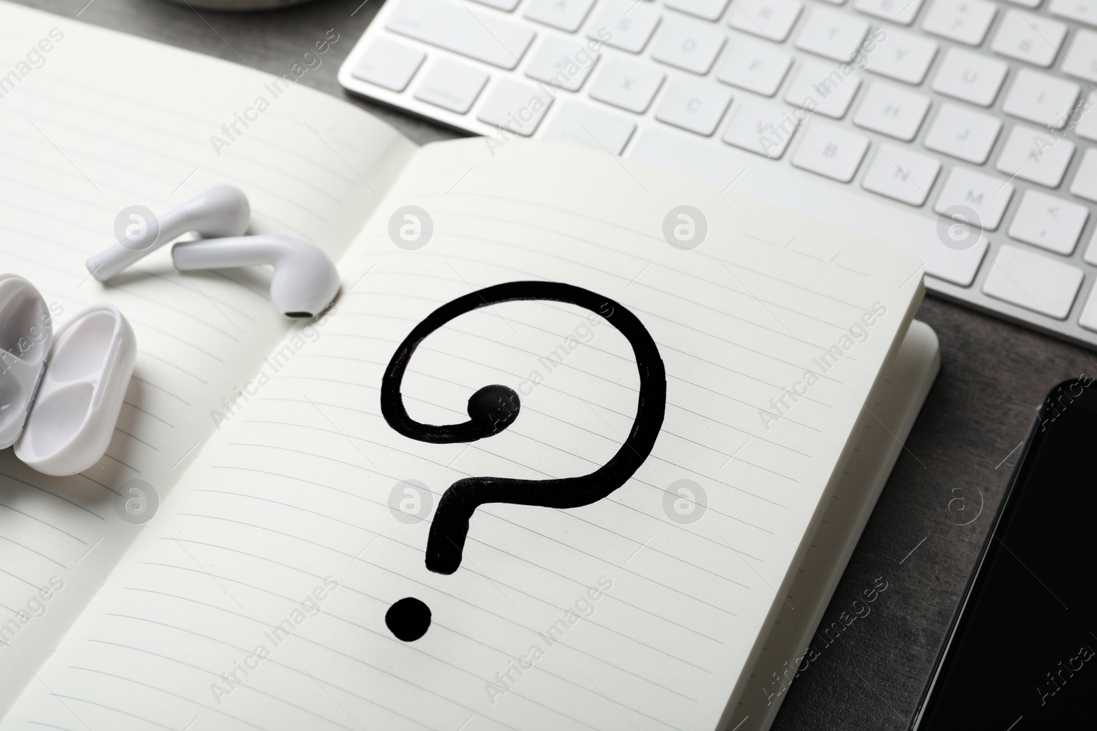 Photo of Notebook with question mark and earphones on grey table, closeup