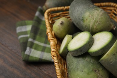 Photo of Green daikon radishes in wicker basket on wooden table, closeup. Space for text