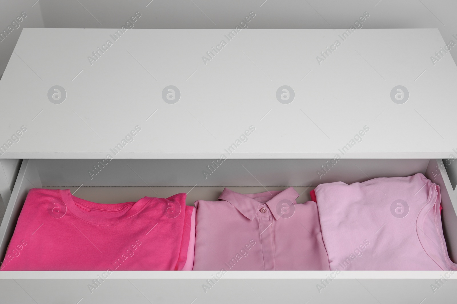 Photo of Many folded pink clothes in white chest of drawers indoors