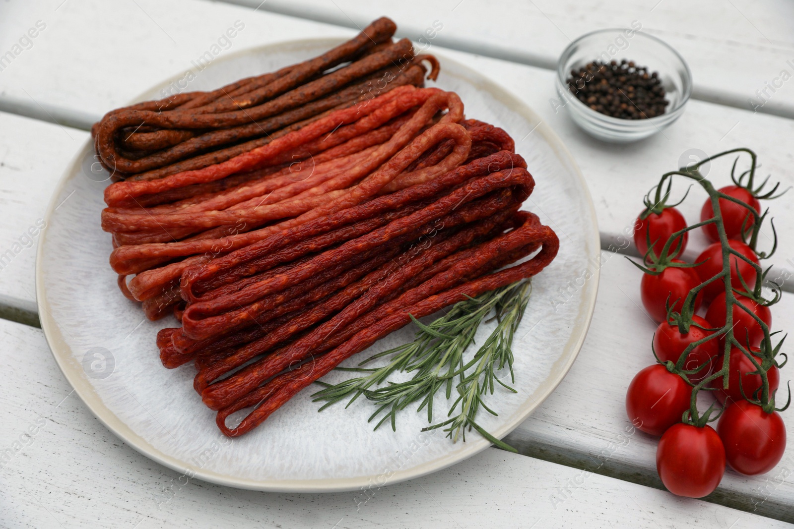 Photo of Delicious kabanosy with rosemary, tomatoes and peppercorn on white wooden table