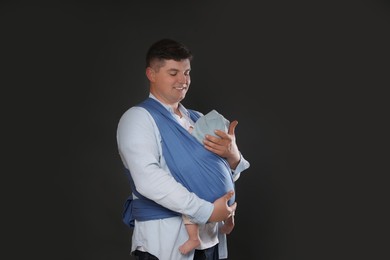 Photo of Father holding his child in sling (baby carrier) on black background. Space for text