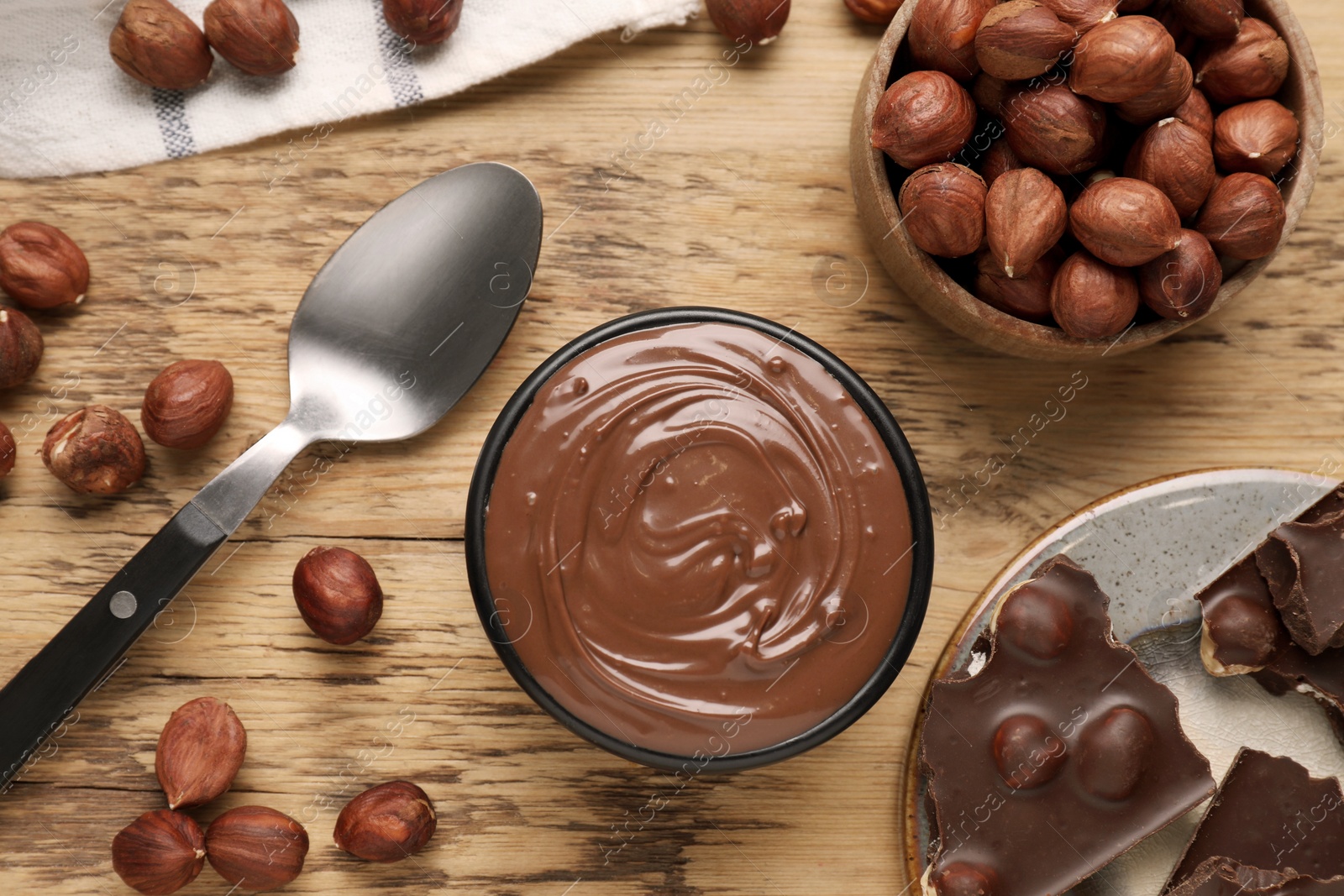 Photo of Chocolate pieces, bowl of sweet paste and nuts on wooden table, flat lay