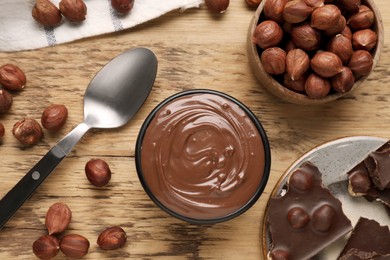 Photo of Chocolate pieces, bowl of sweet paste and nuts on wooden table, flat lay