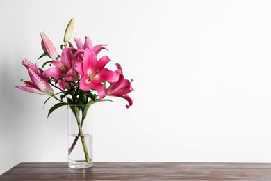 Photo of Beautiful pink lily flowers in vase on wooden table against white background, space for text