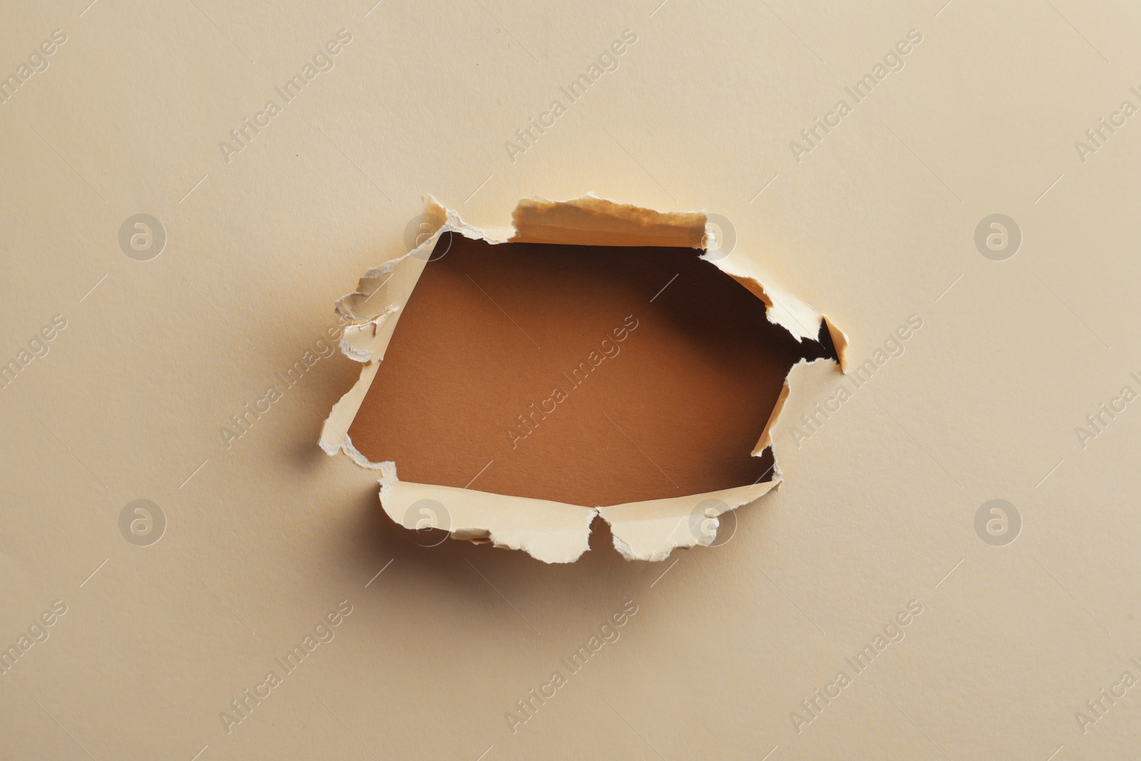 Photo of Hole in light beige paper on brown background