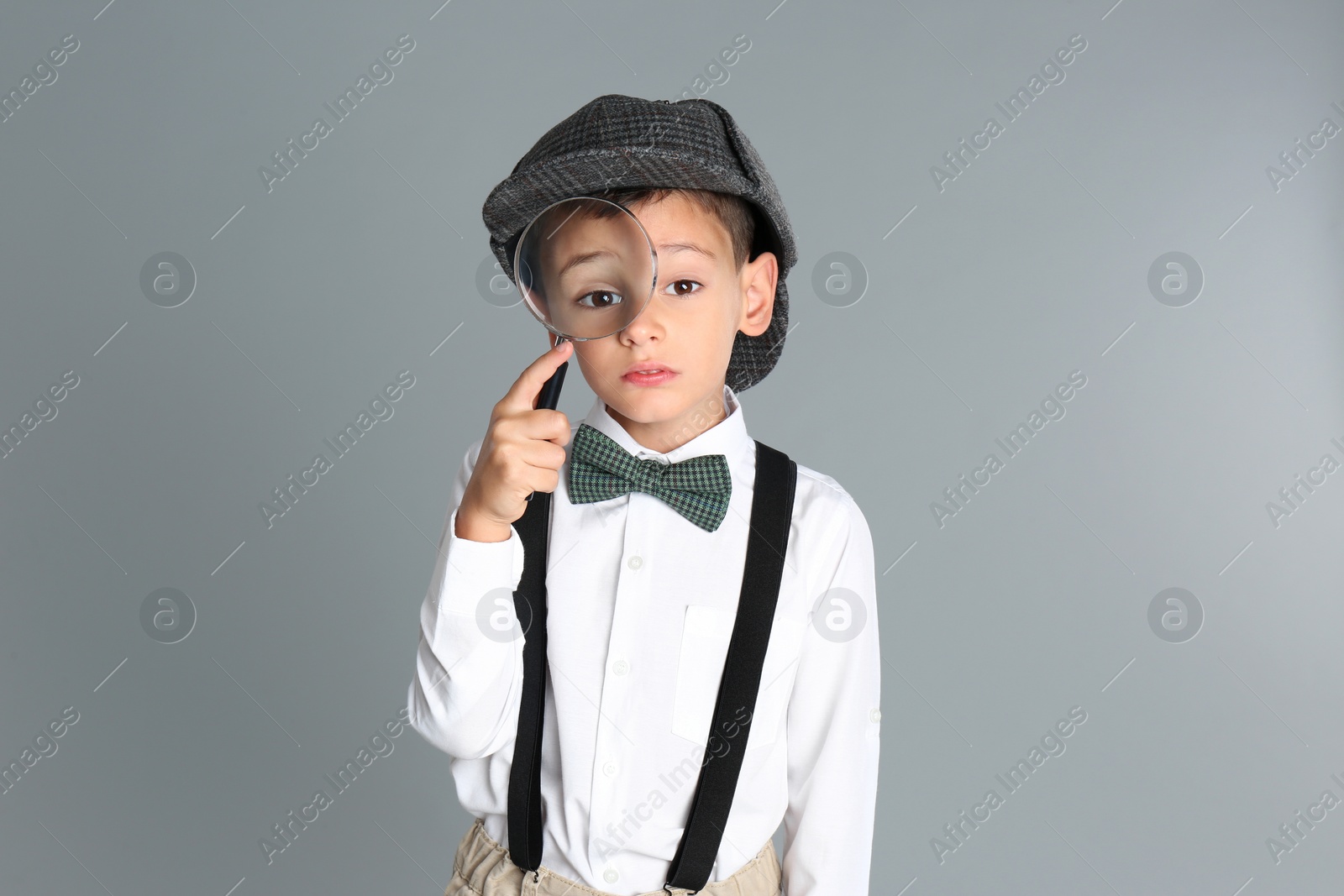 Photo of Little boy with magnifying glass playing detective on grey background