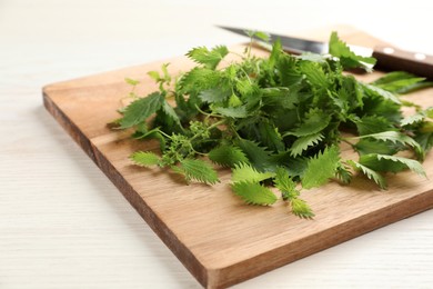 Photo of Wooden board with fresh stinging nettle leaves on white table, closeup