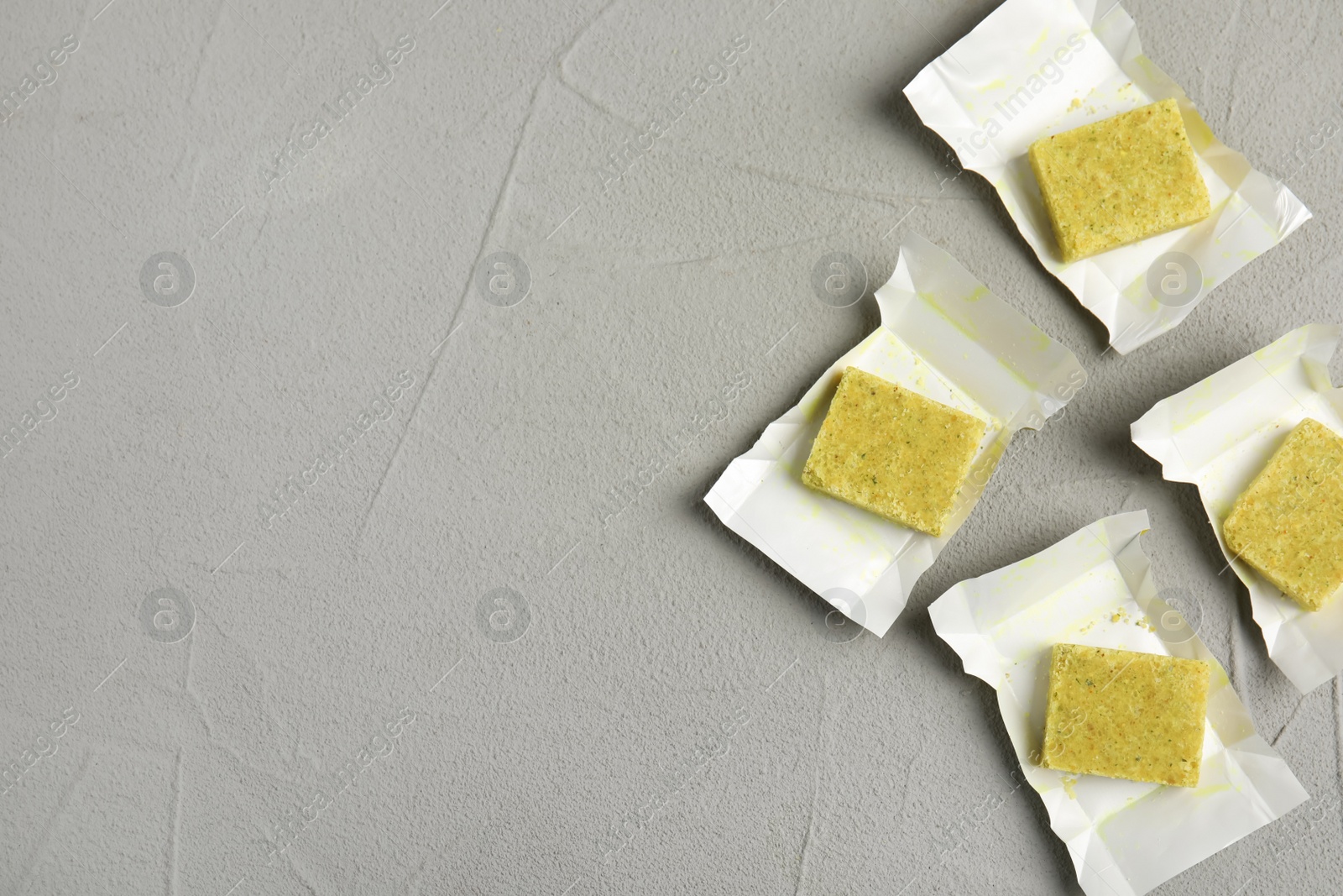 Photo of Bouillon cubes with wraps on light grey table, flat lay. Space for text