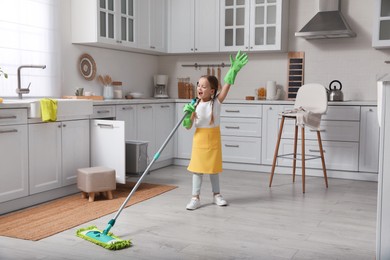 Photo of Cute little girl with mop singing while cleaning at home