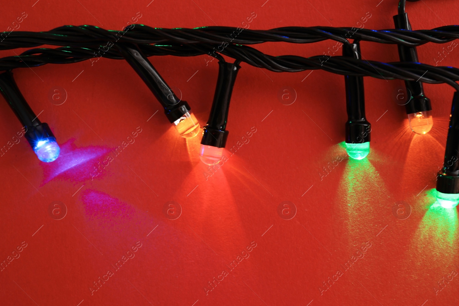 Photo of Glowing Christmas lights on color background, closeup