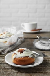 Tasty cinnamon roll with cream on wooden table. Space for text