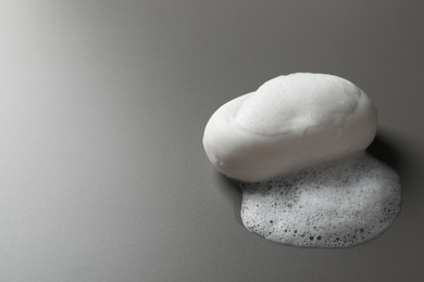 Soap with fluffy foam on grey background, space for text