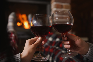 Photo of Couple with glasses of red wine near burning fireplace, closeup