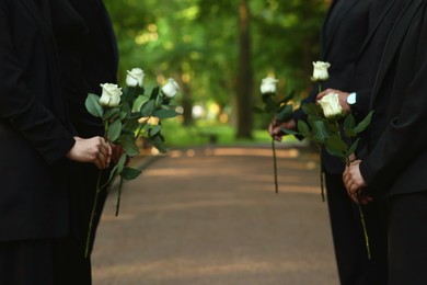 Photo of People with white rose flowers outdoors, closeup. Funeral ceremony