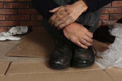 Photo of Poor man wearing old dirty shoes sitting on floor