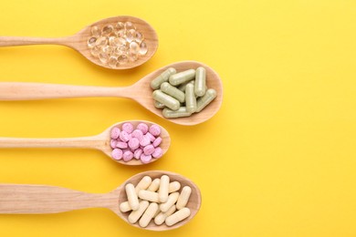 Photo of Different vitamin pills in wooden spoons on yellow background, flat lay. Space for text
