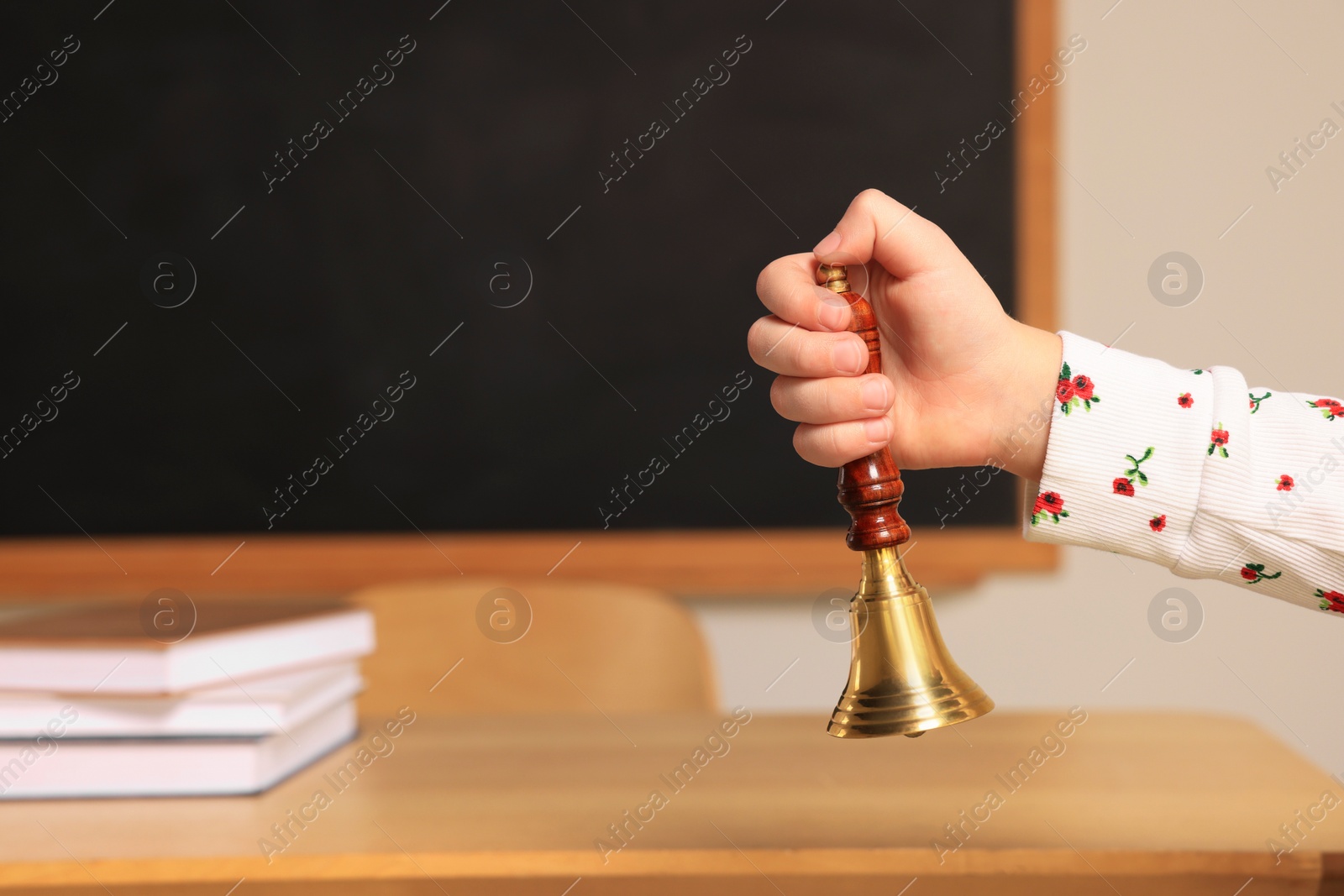 Photo of Pupil with school bell near desk and chalkboard in classroom, closeup. Space for text