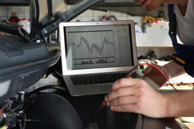 Photo of Mechanic with laptop doing car diagnostic at automobile repair shop, closeup