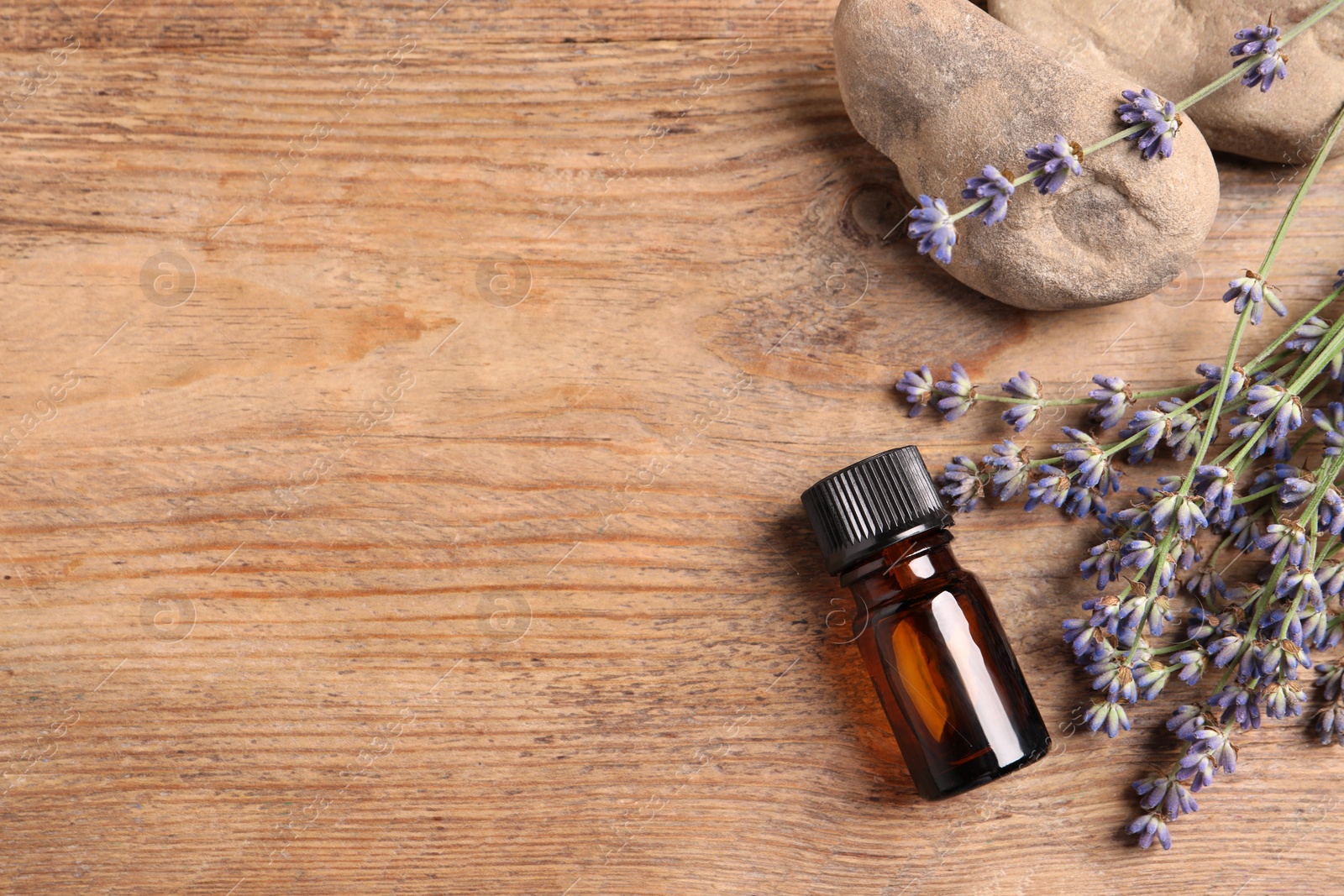 Photo of Bottle of essential oil and lavender flowers on wooden table, flat lay. Space for text