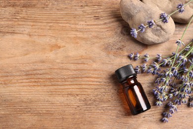 Bottle of essential oil and lavender flowers on wooden table, flat lay. Space for text