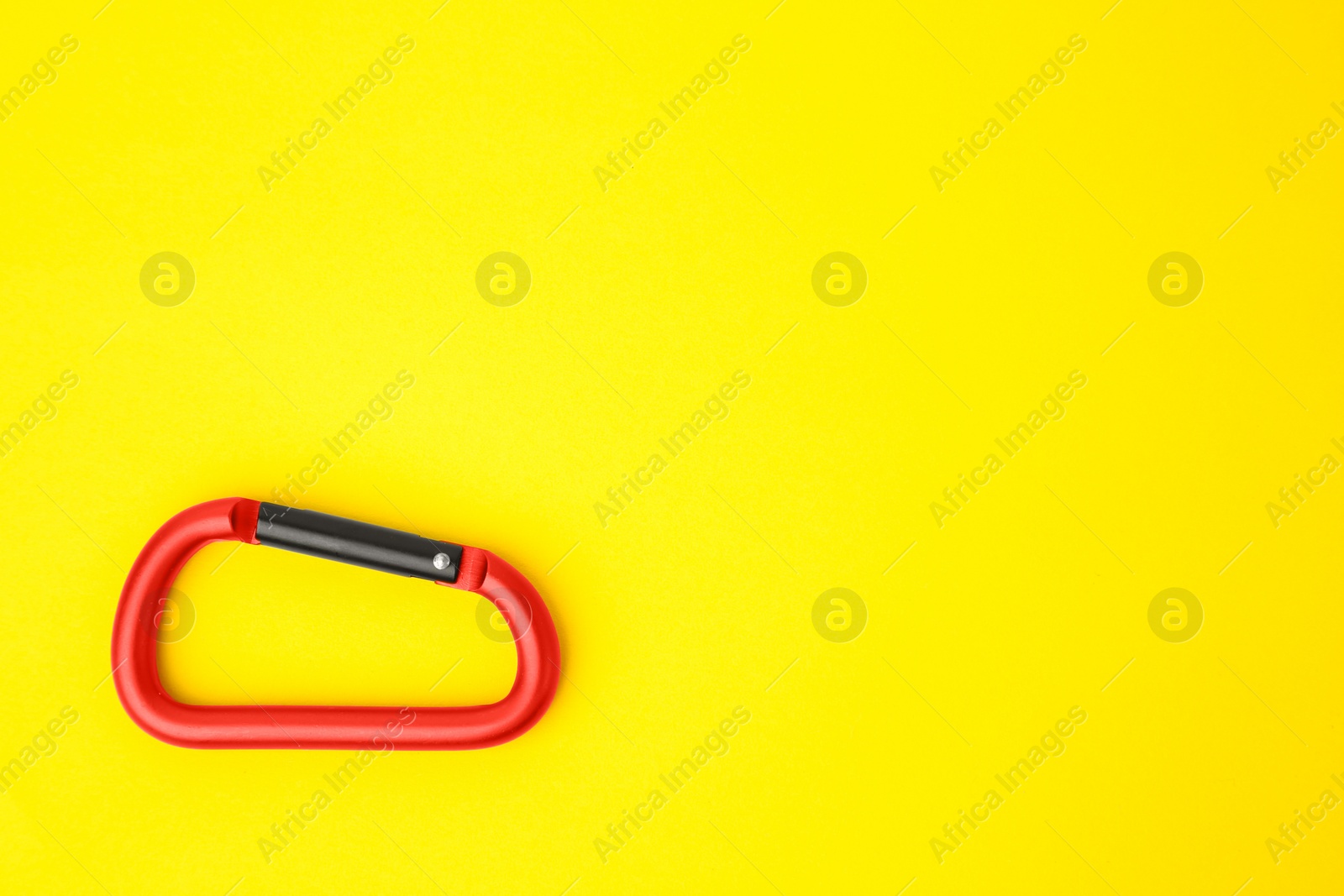 Photo of One red carabiner on yellow background, top view. Space for text