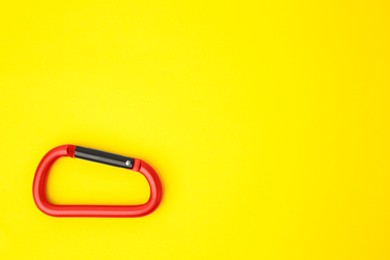 Photo of One red carabiner on yellow background, top view. Space for text