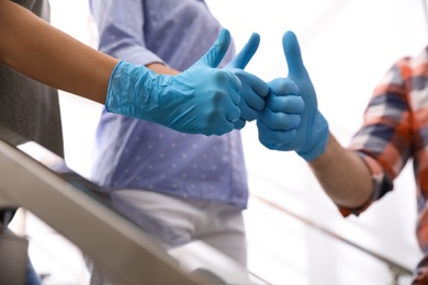 Photo of Group of people in blue medical gloves showing thumbs up on light background, closeup