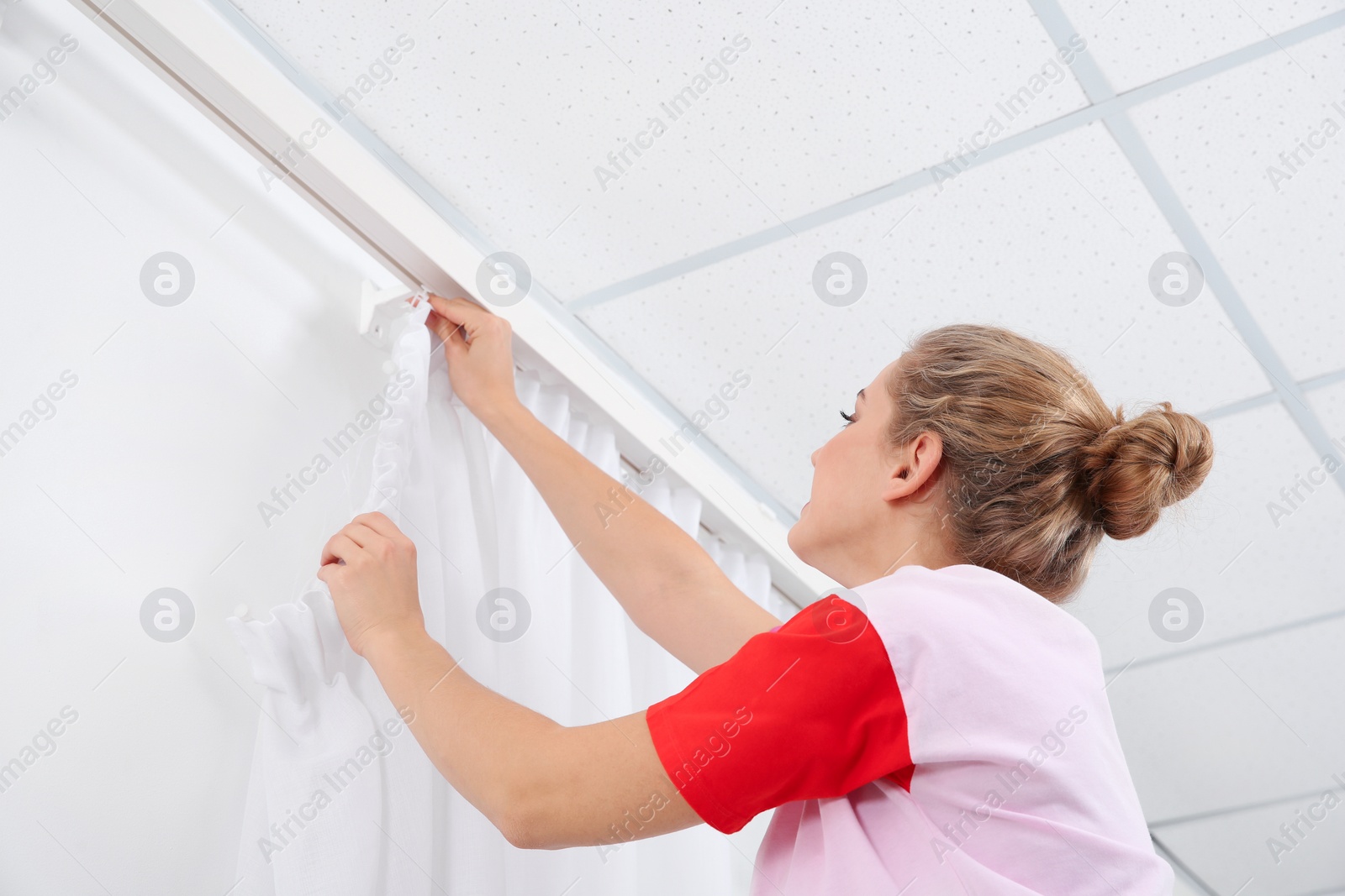 Photo of Woman hanging window curtain indoors. Interior decor element