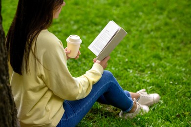 Photo of Young woman with cup of coffee reading book in park